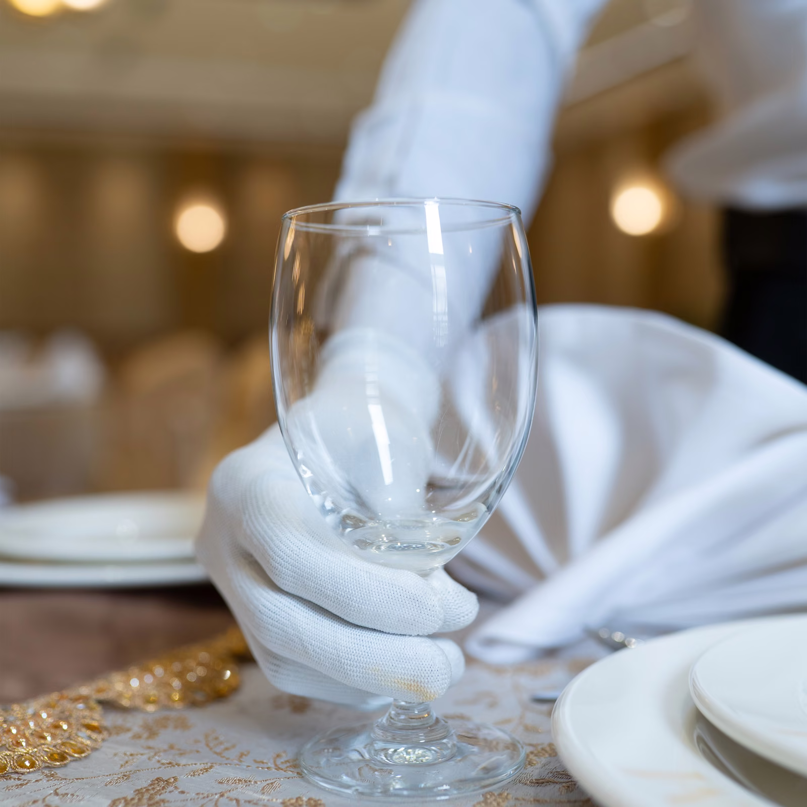 White-gloved steward placing a wine glass at a set table